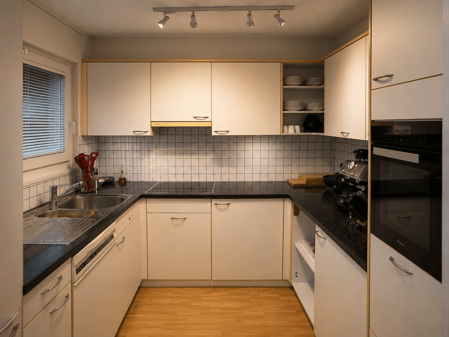 Alte cremefarbene U-Küche mit hellen Holzfronten und gemustertem Fliesenspiegel vor dem Umbau.